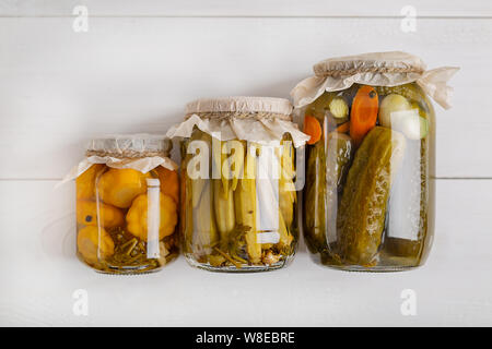 Salatura vari ortaggi in vasetti di vetro per lo stoccaggio a lungo termine. Conserve di verdure in vasi di vetro bianco su sfondo di legno. Vista dall'alto. Foto Stock