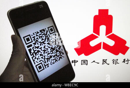 Un Cinese di utenti di telefonia mobile mostra uno smartphone visualizzando un codice QR di fronte un logo della Banca Popolare di Cina (PBOC), la Cina della banca centrale in Foto Stock