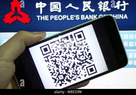 Un Cinese di utenti di telefonia mobile mostra uno smartphone visualizzando un codice QR di fronte un logo della Banca Popolare di Cina (PBOC), la Cina della banca centrale in Foto Stock