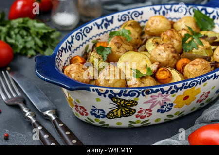 I giovani di patate al forno con zucchine, carote e fagiolini, si trova in una forma di ceramica, contro uno sfondo scuro, orientamento orizzontale, close-up Foto Stock