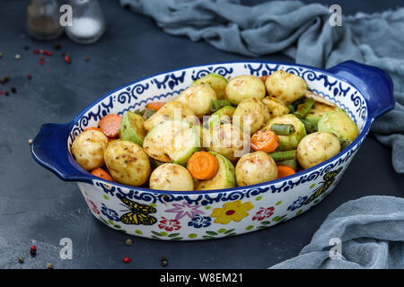 I giovani di patate al forno con zucchine, carote e fagiolini, si trova in una forma di ceramica, contro uno sfondo scuro, orientamento orizzontale, close-up Foto Stock