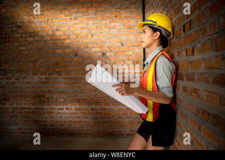 Ingegnere asiatica donna con blueprint con muro di mattoni in background Foto Stock