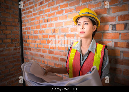 Ingegnere asiatica donna con blueprint con muro di mattoni in background Foto Stock