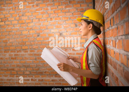 Ingegnere asiatica donna con blueprint con muro di mattoni in background Foto Stock