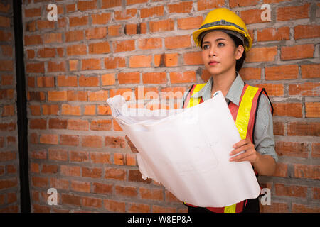 Ingegnere asiatica donna con blueprint con muro di mattoni in background Foto Stock