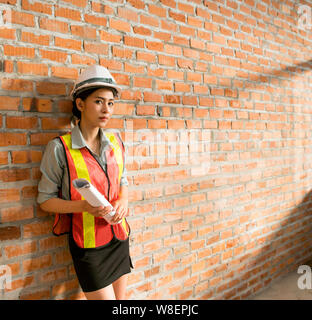 Ingegnere asiatica donna con blueprint con muro di mattoni in background Foto Stock