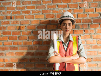 Ingegnere asiatica donna con blueprint con muro di mattoni in background Foto Stock