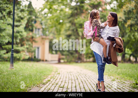 Sorridente madre tenendo una figlia con zainetto è in posizione di parcheggio Foto Stock