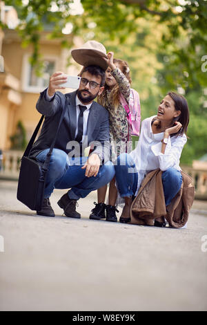 Primo giorno di scuola e genitori felici e ragazza facendo una foto di fronte a scuola Foto Stock