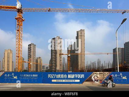 --FILE--ciclisti cinese di guidare la propria bicicletta elettrica passato il cantiere per la costruzione di immobili residenziali progetto nella città di Huaian, est della Cina di Jiangsu pr Foto Stock