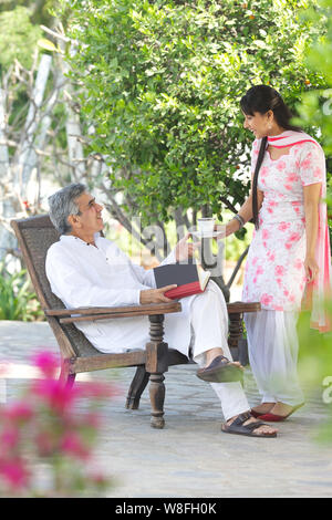 Giovane donna che serve il tè al padre seduto in giardino Foto Stock