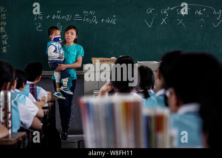Zhang Wei porta il suo 3-anno-vecchio figlio Tutu, chi soffre di leucemia, mentre dà una lezione di chimica in un' aula a Hanshou n. 1 Alta scuola Foto Stock