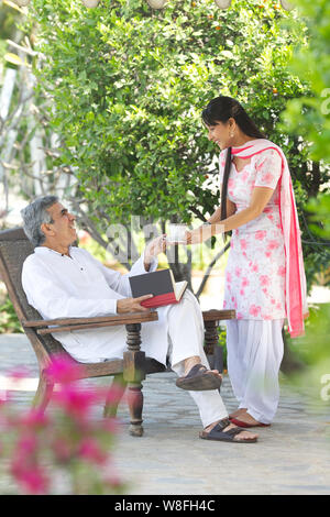 Giovane donna che serve il tè al padre seduto in giardino Foto Stock