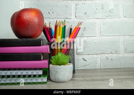 Torna a scuola con il concetto di pila di libri, rosso apple, pianta in vaso e matite contro un bianco muro di mattoni con libero spazio di copia Foto Stock