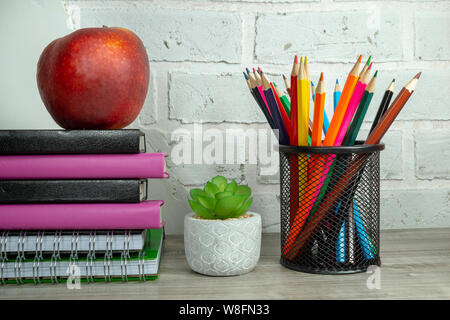 Torna a scuola con il concetto di pila di libri, rosso apple, pianta in vaso e matite contro un bianco muro di mattoni con libero spazio di copia Foto Stock