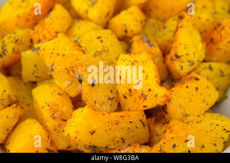 Fette di zucca al forno, deliziosi cubetti di polpa di zucca con spezie ed erbe aromatiche, sfondo. Fotografia di cibo, verdura cotta ve vegetariano Foto Stock