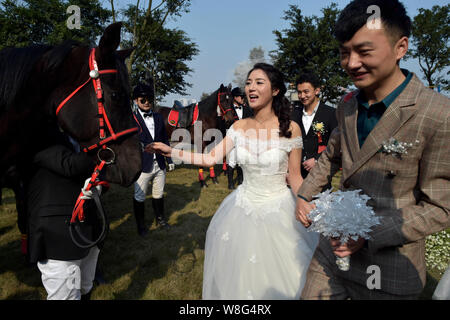 Una sposa giovane che sono sia gli amanti dei cavalli a piedi passato equestrians con i cavalli durante la loro cerimonia di nozze a Chongqing Cina, 7 marzo 2015. Un nuovo Foto Stock