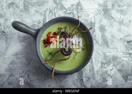 Vista superiore zuppa di asparagi con il polpo in una ciotola grigio su un marmo cemento grigio. Spazio di copia, cibo foto pubblicità, luce morbida. Foto Stock