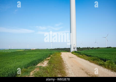 Il paesaggio della murgia con la strada in direzione di una turbina eolica. Regione Puglia, Italia Foto Stock