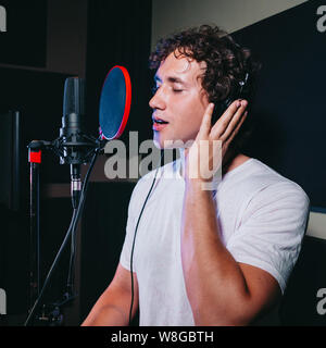 Un espressivo uomo che canta una canzone in un microfono in uno studio di registrazione. Foto Stock