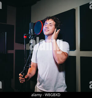 Un espressivo uomo che canta una canzone in un microfono in uno studio di registrazione. Foto Stock