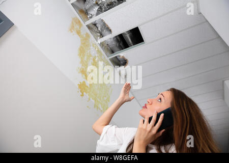 Triste Donna che chiama idraulico mentre guarda il massimale delle perdite in corridoio Foto Stock