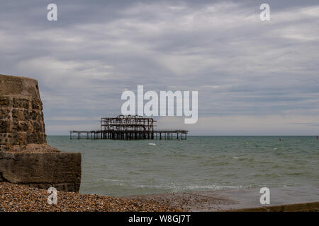 Una vista dei rovinato Molo Ovest di Brighton beach in grigio di una giornata estiva, Sussex, Inghilterra Foto Stock