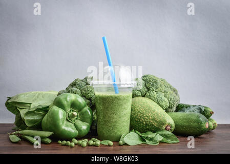 Blended frullato verde in una tazza di plastica con ingredienti sul tavolo di legno Foto Stock