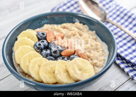 Ciotola di porridge di fiocchi d'avena con banana, mirtilli, mandorle, su sfondo di legno Foto Stock