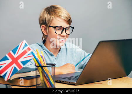 Sorridente schoolboy in bicchieri studiare inglese dal portatile Foto Stock