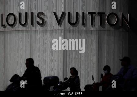 --FILE--ciclisti corsa biciclette elettriche passato una boutique alla moda di Louis Vuitton (LV) in Cina a Shanghai, 12 maggio 2015. Per contrastare il calo delle vendite in th Foto Stock