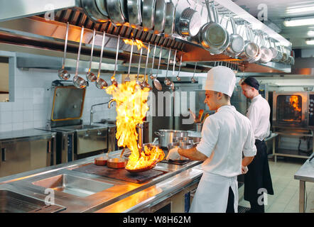 Cucina moderna. I cuochi preparano pasti sul fornello nella cucina del ristorante o albergo. Il fuoco in cucina. Foto Stock