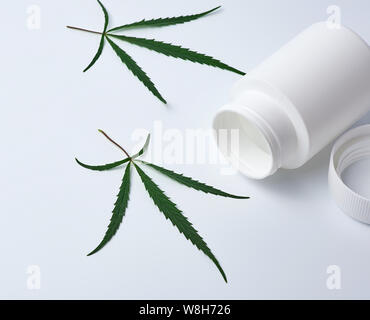 Aprire il vuoto in plastica bianca medical jar per pillole e verde foglia di canapa su uno sfondo bianco, medicina alternativa nozione Foto Stock