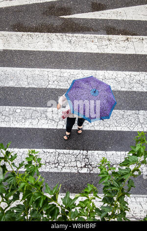 Scena di una donna con la moda ombrello attraversando il marciapiede. Vista dall'alto. Rainy day concept Foto Stock