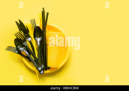 Picnic monouso nero coltello e forche su giallo. Vista dall'alto. Lay piatto. Rifiuti Zero, salvare il pianeta, pericolo di plastica. Foto Stock