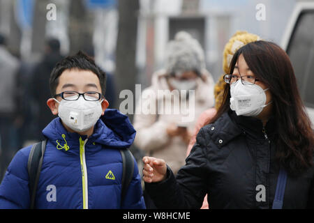 Pedoni indossando maschere viso a piedi su una strada di smog pesante a Pechino in Cina, 8 dicembre 2015. Foto Stock