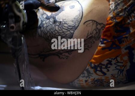 Chinese tattoo artist Wang Wenbin inchiostri la coscia di un cliente in un tattoo studio in Cina a Shanghai, 29 marzo 2015. In un tattoo studio a Shanghai Foto Stock