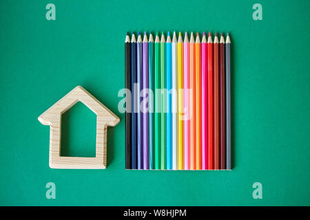 Una casa in legno e figurine diverse matite colorate isolare su sfondo verde, concetto torna a scuola, il fuoco selettivo Foto Stock