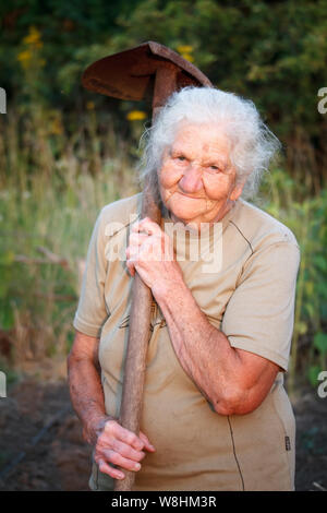Closeup ritratto di una vecchia donna con i capelli grigi sorridenti e guardando la telecamera, tenendo in mano una pala arrugginito nelle sue mani, faccia in profonde rughe, selet Foto Stock
