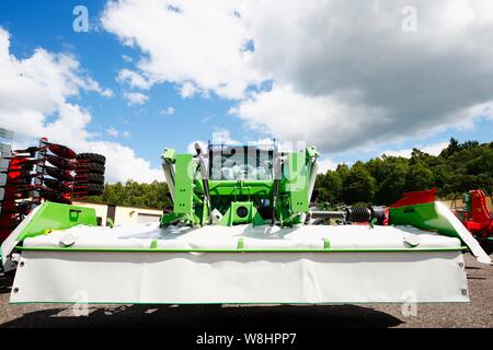 Trattrice agricola con grandi macchine tosaerba accoppiato alla parte anteriore con l'impianto idraulico. Foto Stock