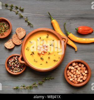 Zuppa di zucca in vaso in ceramica su grigio legno rustico servita con timo e crostini. Accanto ad essa sono il peperoncino, foglie di timo e crostini. Piatto, laici vi Foto Stock
