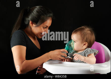 Happy baby ragazza con maschera di inalazione isolati su sfondo nero Foto Stock