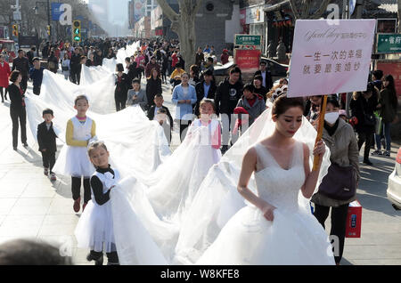 Un modello che indossa un abito nuziale con un 101-metro-long tail portati dai ragazzi e i membri del personale di un abito da sposa azienda sfilate lungo una via d Foto Stock