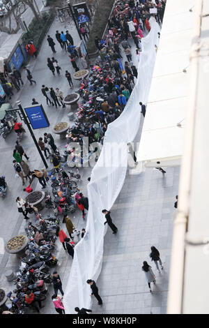 Un modello che indossa un abito nuziale con un 101-metro-long tail portati dai ragazzi e i membri del personale di un abito da sposa azienda sfilate lungo una via d Foto Stock