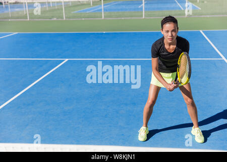 Asian giocatore di tennis donna pronto per la riproduzione su disco blu corte scoperta in estate in posizione azienda racket indossa vestito con grembiule e scarpe. Atleta femminile la determinazione e il concetto di concentrazione. Foto Stock