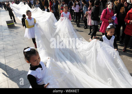 I ragazzi e i membri del personale di un abito da sposa azienda portano il 101-metro-lunga coda di un abito nuziale tutto visualizzato da un modello sfilando lungo una strada Foto Stock