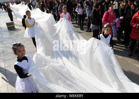 I ragazzi e i membri del personale di un abito da sposa azienda portano il 101-metro-lunga coda di un abito nuziale tutto visualizzato da un modello sfilando lungo una strada Foto Stock