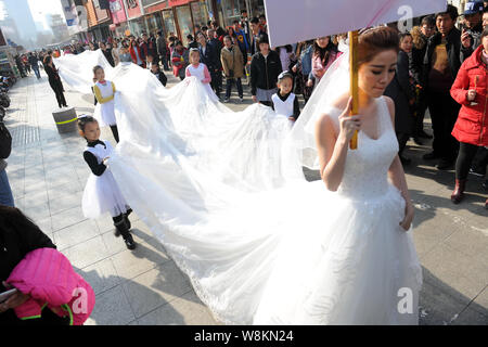 Un modello che indossa un abito nuziale con un 101-metro-long tail portati dai ragazzi e i membri del personale di un abito da sposa azienda sfilate lungo una via d Foto Stock