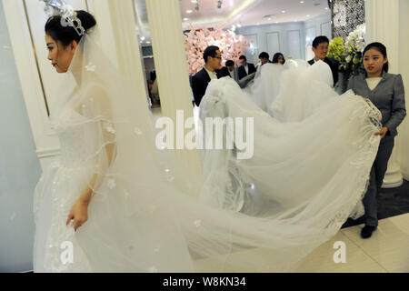 Un modello che indossa un abito nuziale con un 101-metro-long tail trasportati dai membri del personale di un abito da sposa azienda passeggiate fuori di un negozio della società bef Foto Stock