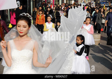 Un modello che indossa un abito nuziale con un 101-metro-long tail portati dai ragazzi e i membri del personale di un abito da sposa azienda sfilate lungo una via d Foto Stock